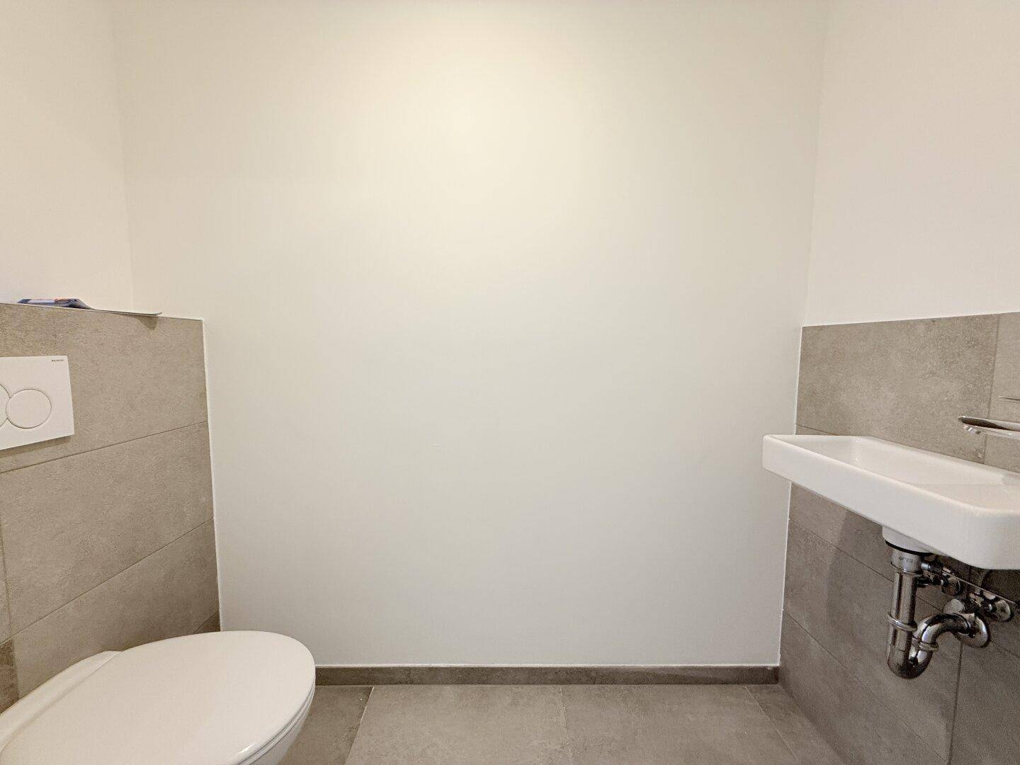 Modernes Gäste-WC mit Wand-WC, kleinem Waschbecken und grauen Fliesen an Wänden und Boden.