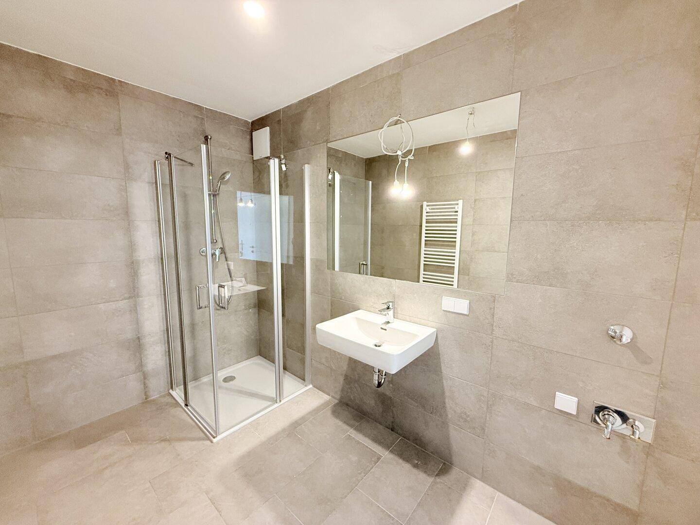 Modernes Badezimmer mit Duschkabine, Waschbecken und einem großen Wandspiegel über dem Waschtisch.