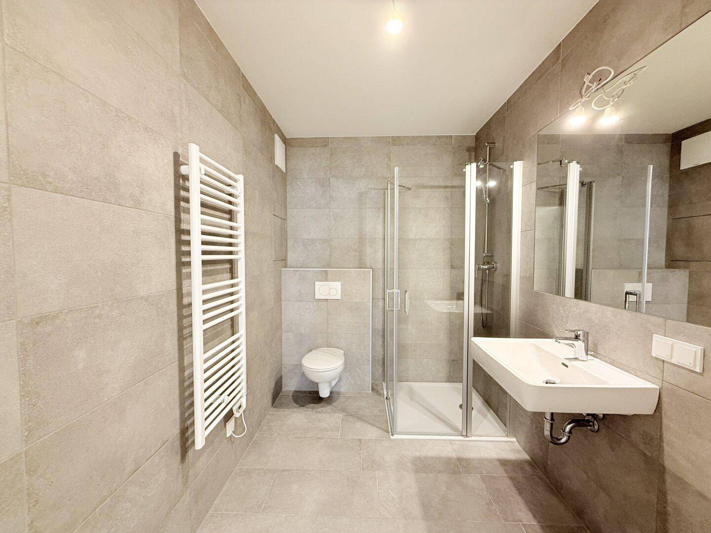 Modernes Badezimmer mit Dusche, Wand-WC, Waschbecken und beheiztem Handtuchhalter.