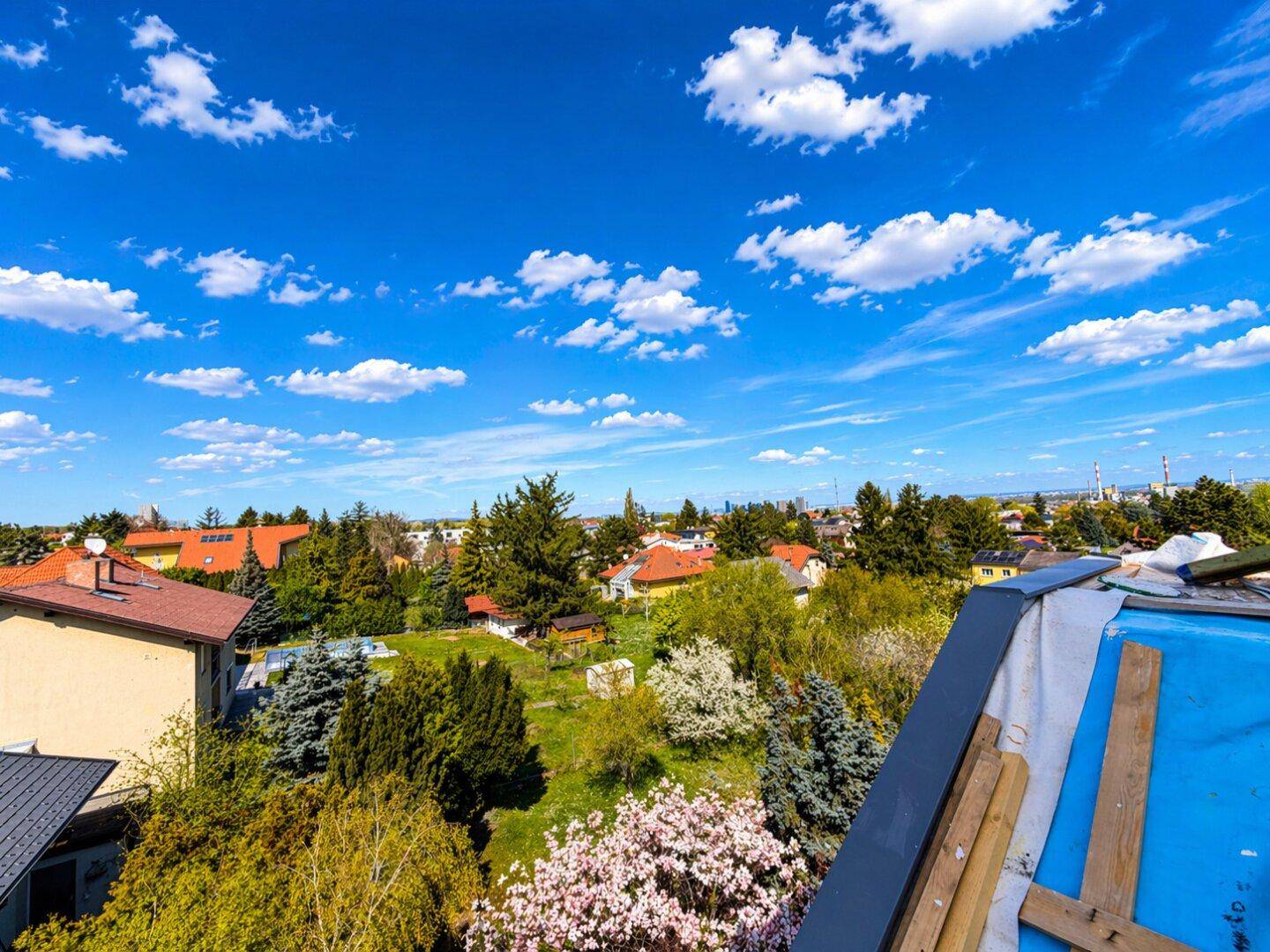 Panoramablick über eine grüne Wohnsiedlung mit Häusern und blühenden Bäumen unter blauem Himmel.