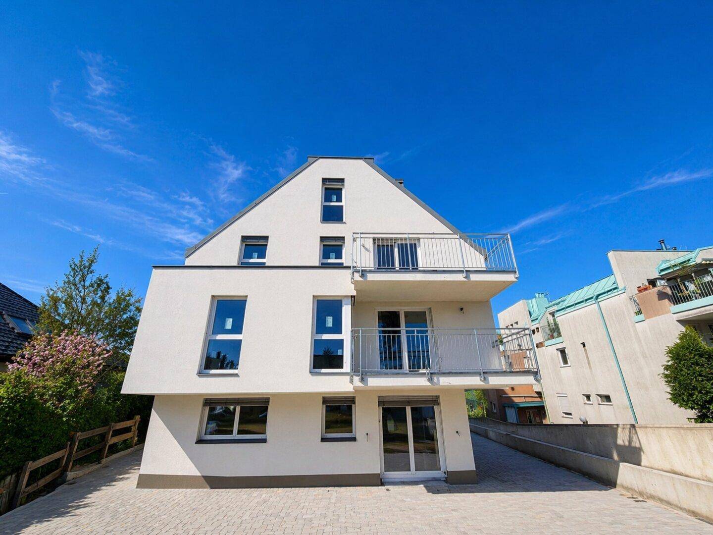 Vorderansicht des modernen weißen Apartmentgebäudes mit Balkonen und großen Fenstern unter klarem Himmel.