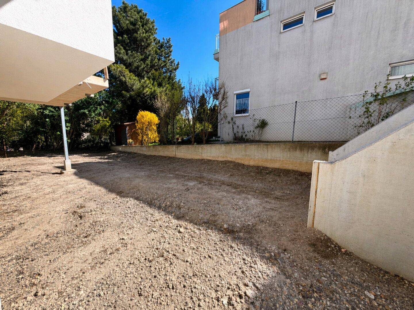 Unfertiger Gartenbereich mit kahlem Boden neben dem Gebäude, bereit für die Landschaftsgestaltung.