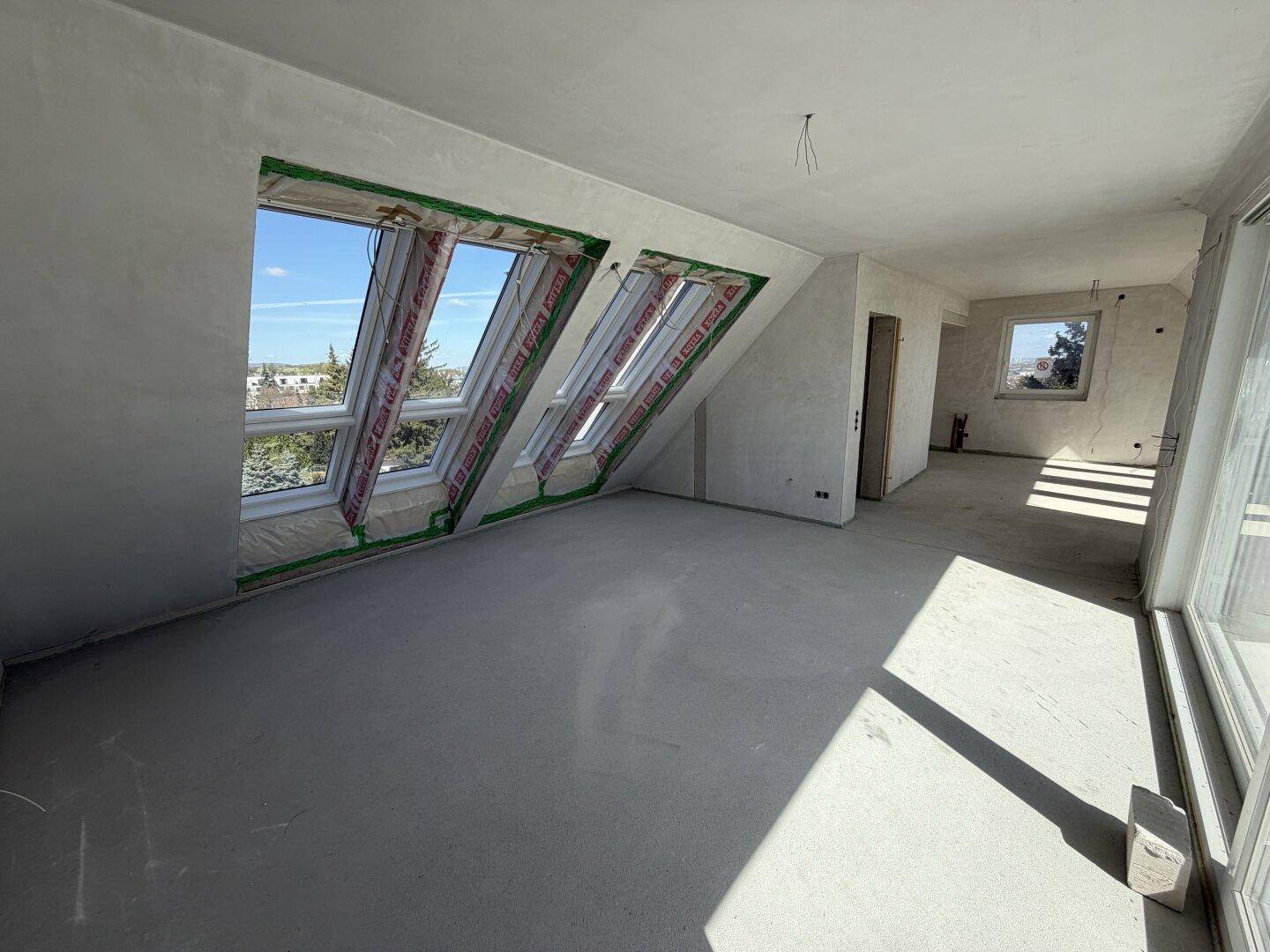 Geräumiger Rohbau-Raum mit schrägen Wänden, Dachfenstern und einem normalen Fenster.