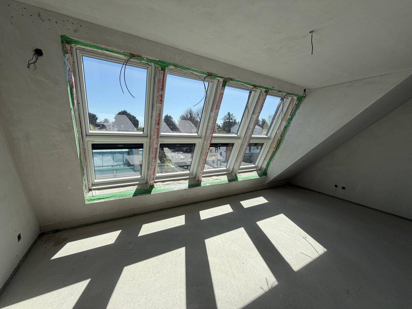 Lichtdurchfluteter Rohbau-Raum im Dachgeschoss mit einer Reihe von schrägen Dachfenstern.