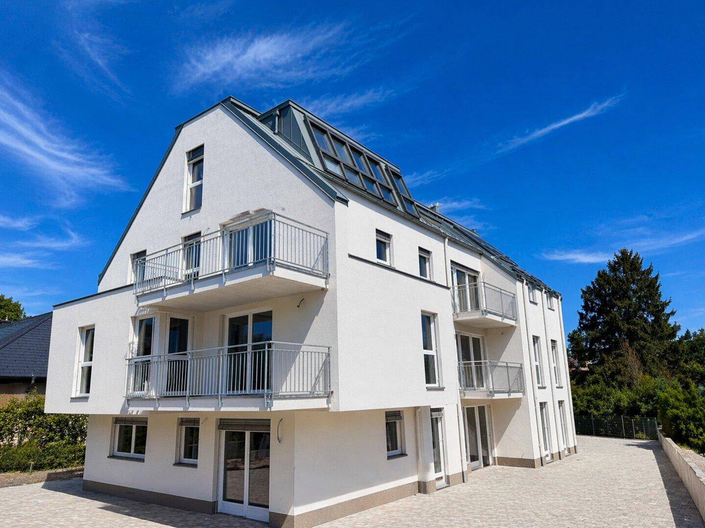 Seitenansicht eines modernen Wohngebäudes mit mehreren Balkonen und Dachfenstern unter blauem Himmel.