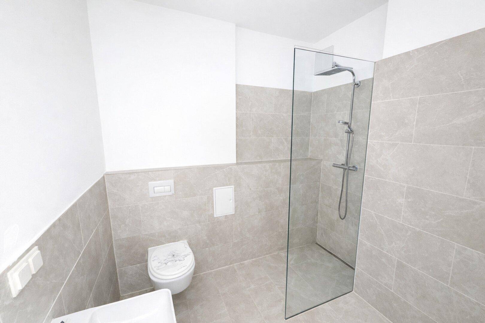 Modernes Badezimmer mit grauen Fliesen, wandhängendem WC und ebenerdiger Dusche.
