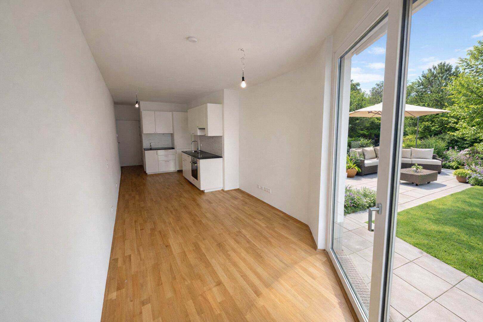 Heller Raum mit kleiner Küchenzeile, Holzboden und Zugang zu einer Terrasse mit Gartenblick.