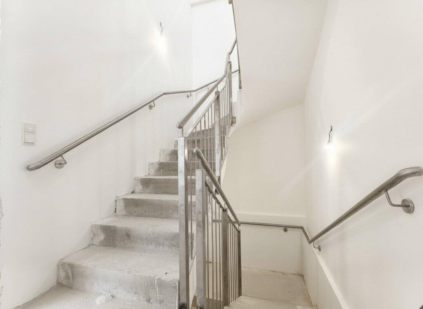 Treppenhaus im Rohbau mit Betonstufen und modernen Edelstahlgeländern.
