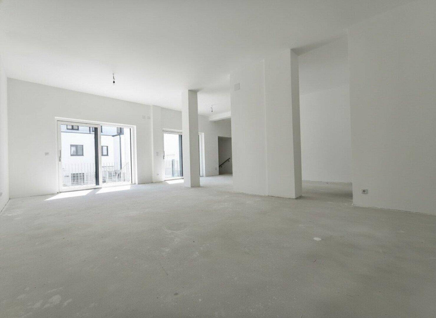 Geräumiger Rohbau-Raum mit viel Tageslicht und Zugang zu einem Balkon.
