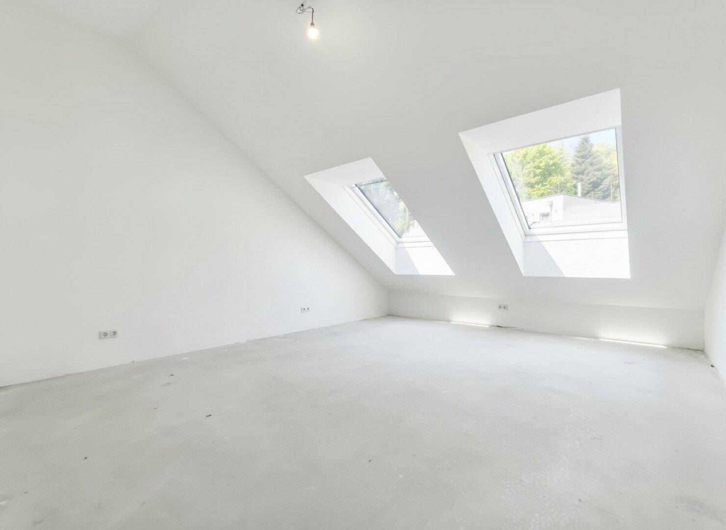 Dachgeschossraum im Rohbau mit zwei Dachfenstern und viel Tageslicht.