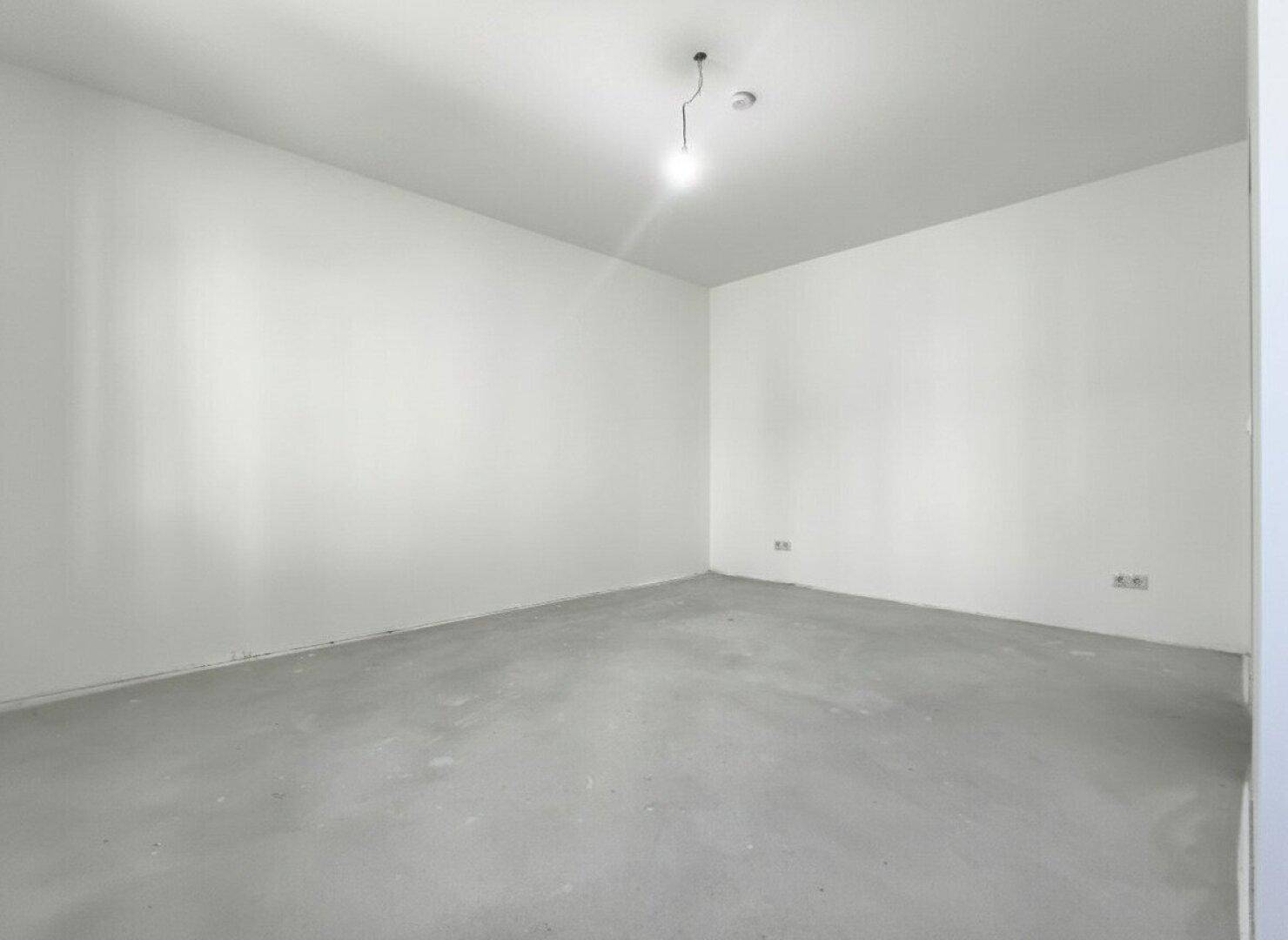 Leerer Raum im Rohbau mit weißen Wänden und Betonboden.
