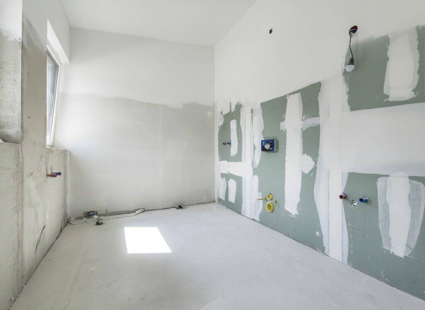 Badezimmer im Rohbau mit sichtbaren Installationen und einem Fenster.