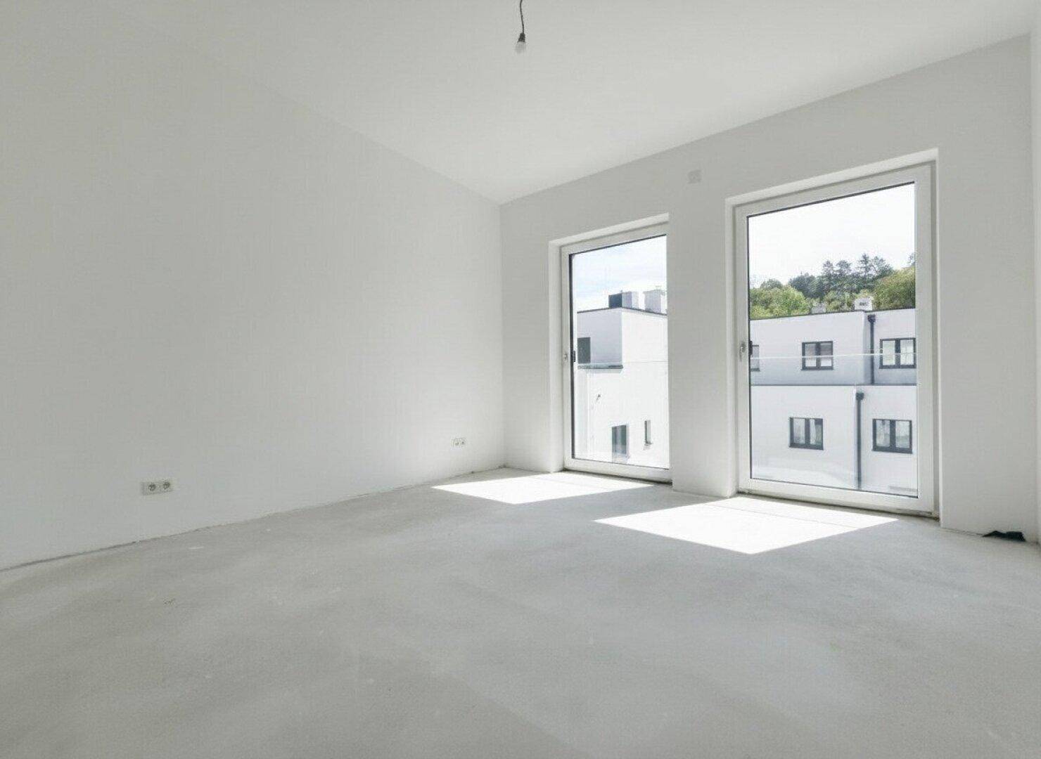 Heller Rohbau-Raum mit großen Fenstern und Blick auf die Nachbargebäude.