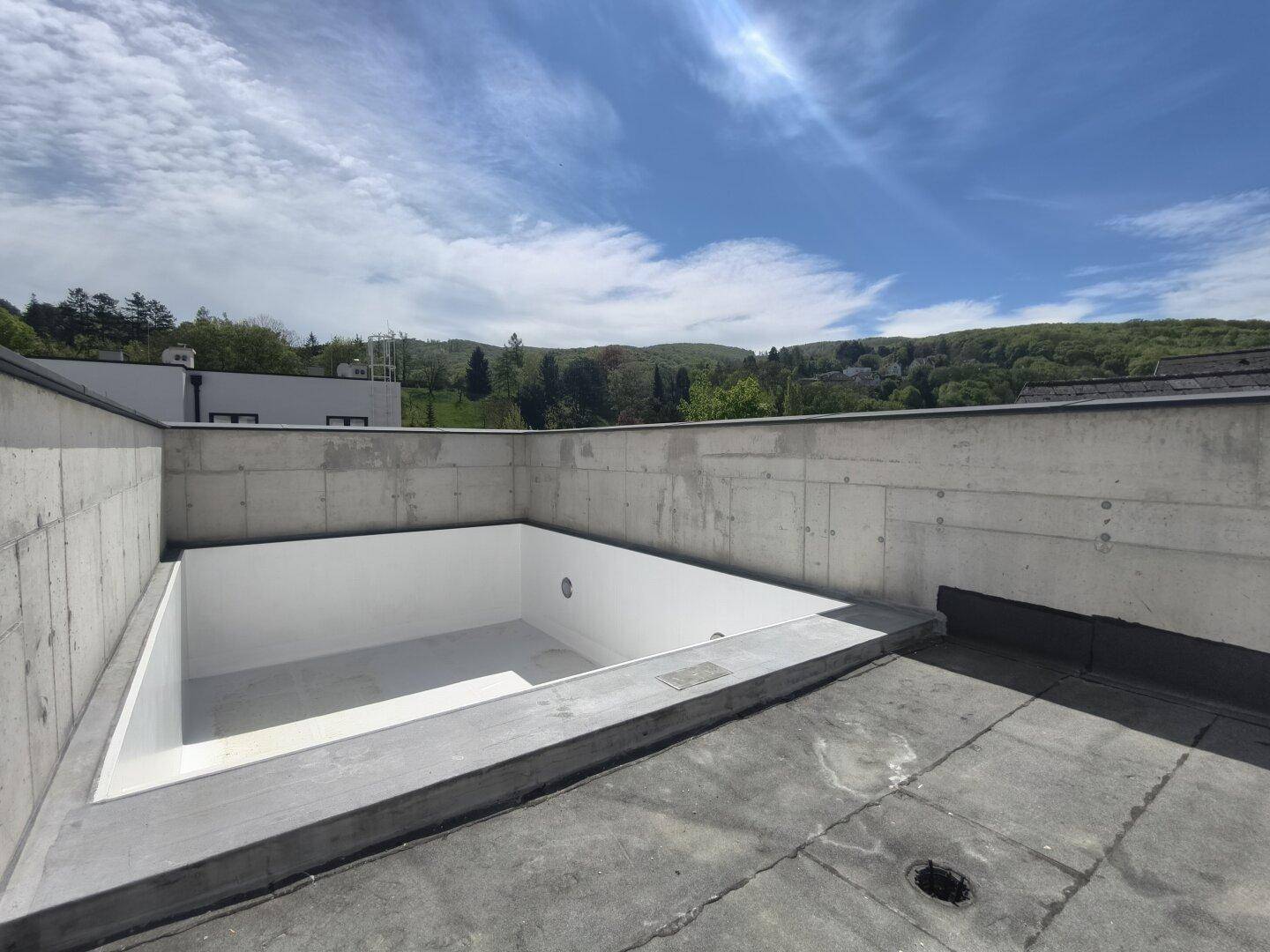 Leeres Schwimmbecken auf einer Dachterrasse mit weitem Blick in die Landschaft.