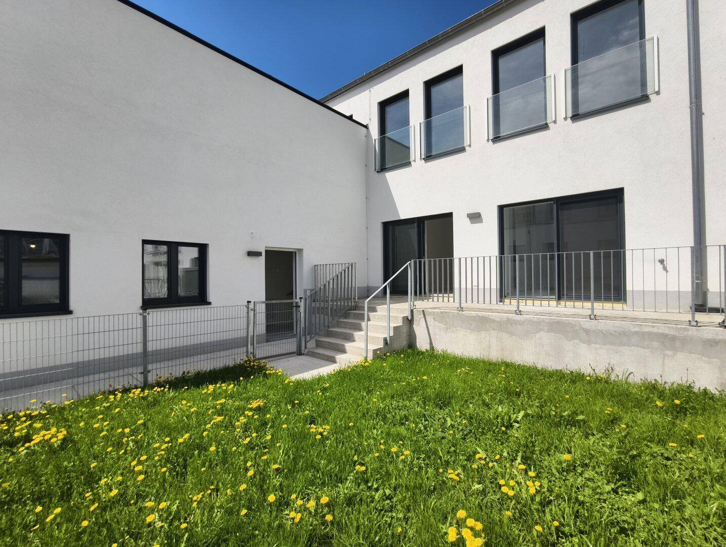 Gartenbereich mit Rasen und Treppe, umgeben von modernen Wohngebäuden.