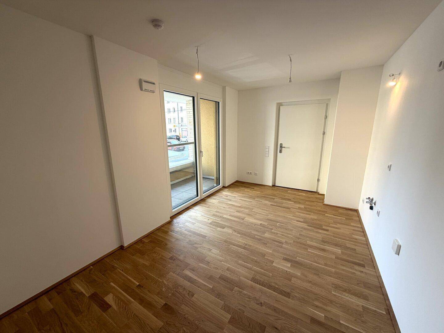 Wohnraum mit Holzboden und Zugang zu einem Balkon, bietet helles und freundliches Ambiente.