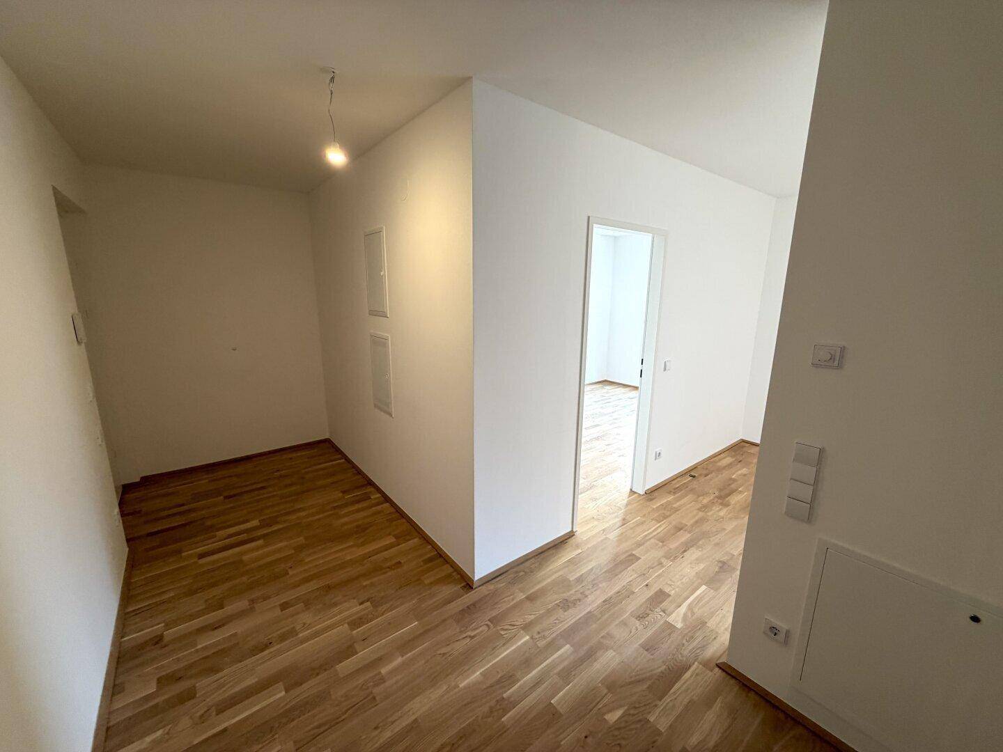 Heller Flur mit Holzboden und weißen Wänden, der zu weiteren Räumen führt.