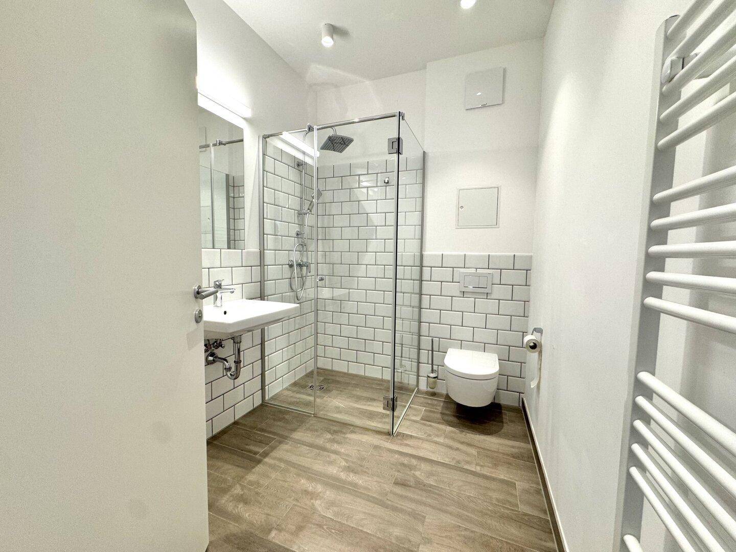 Modernes Badezimmer mit ebenerdiger Dusche, weißen Fliesen und Handtuchheizkörper.