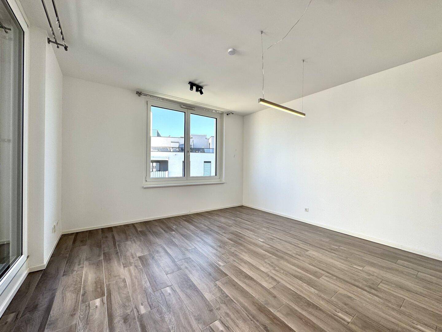 Geräumiges Wohnzimmer mit großen Fenstern, Holzboden und viel natürlichem Licht.