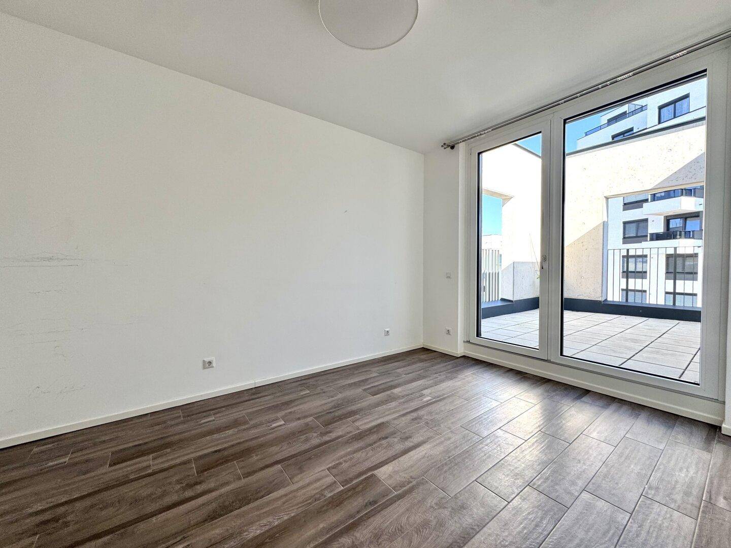 Helles Zimmer mit Holzboden und direktem Zugang zu einer großen Terrasse.