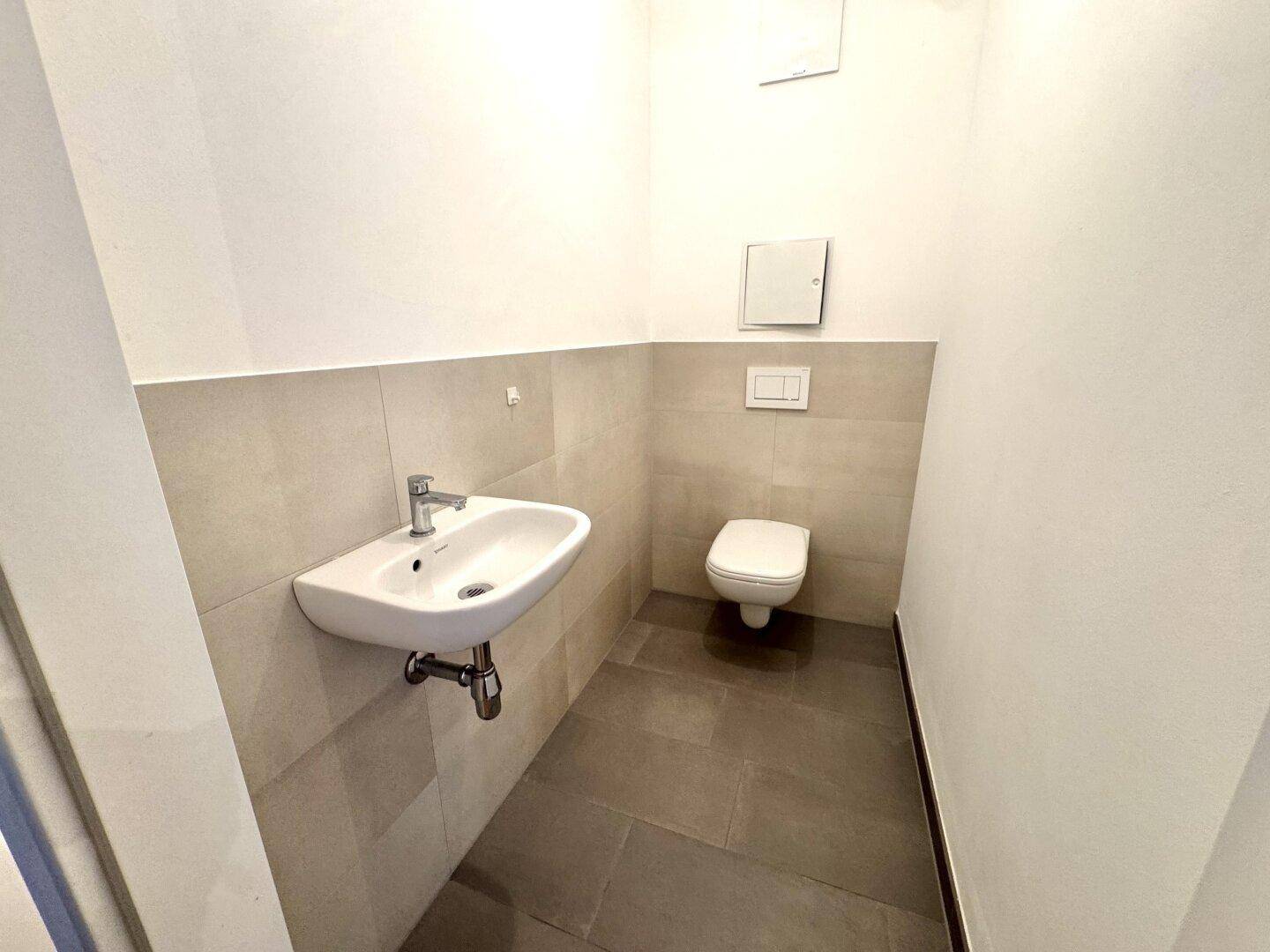 Separates Gäste-WC mit Wand-WC, Waschbecken und modernen Fliesen.