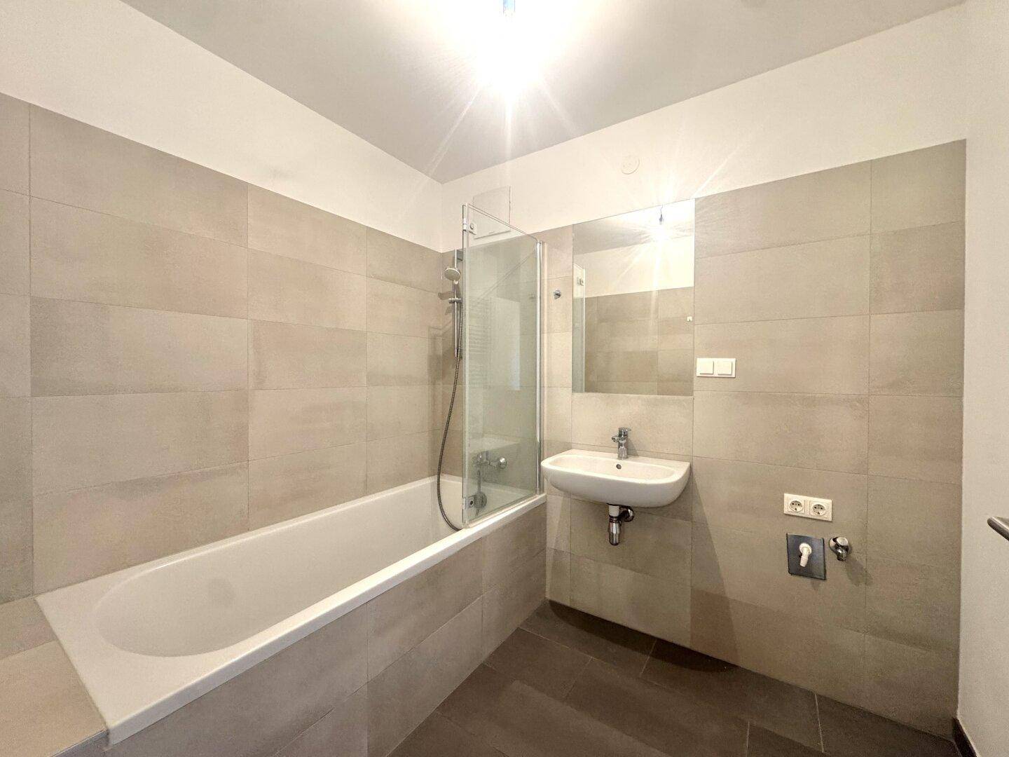 Modernes Badezimmer mit Badewanne, Duschabtrennung und hellen Fliesen an Wänden und Boden.