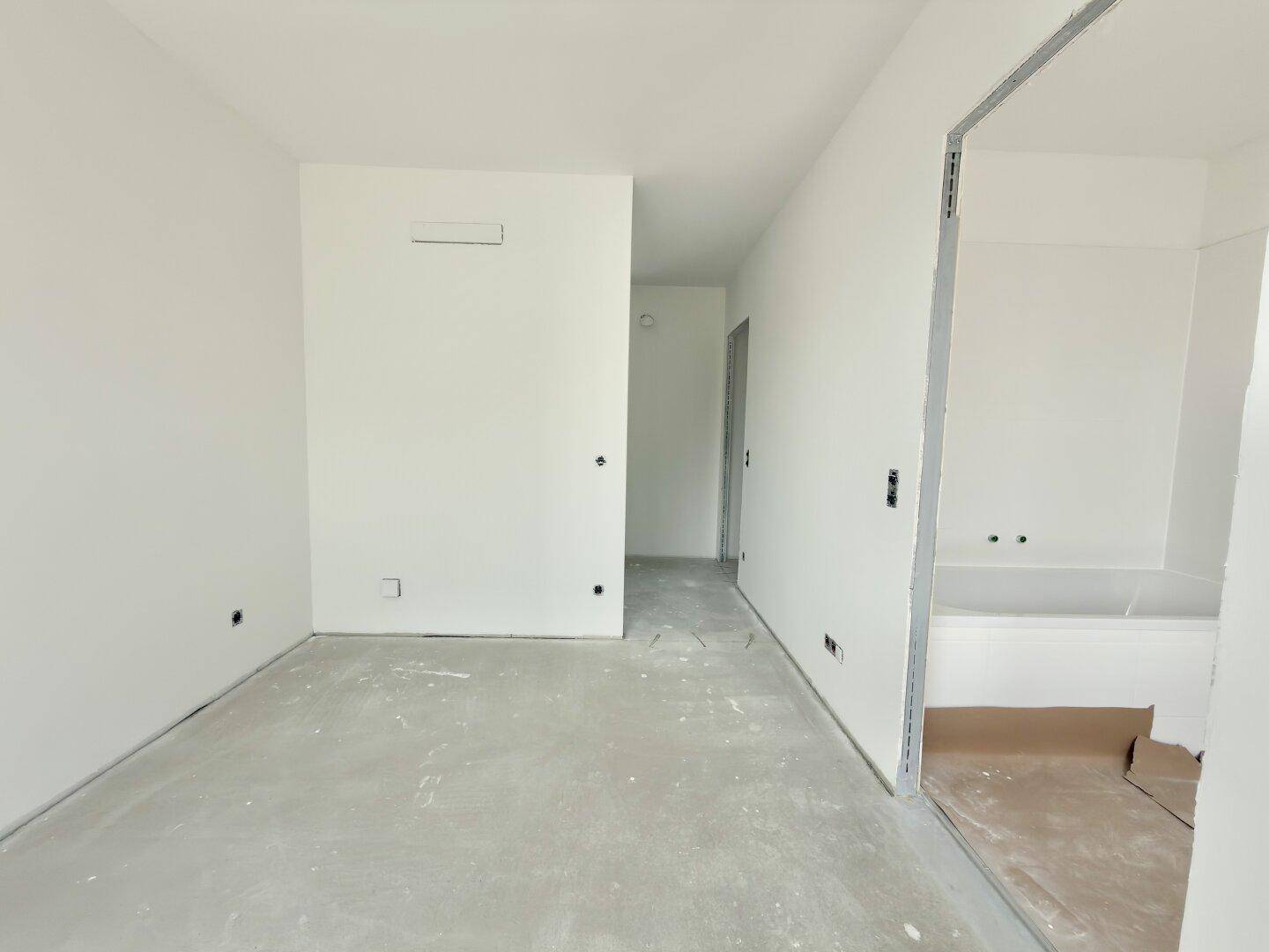 Leerer Raum im Bauzustand mit weiß gestrichenen Wänden und vorbereitetem Bereich für ein Badezimmer.