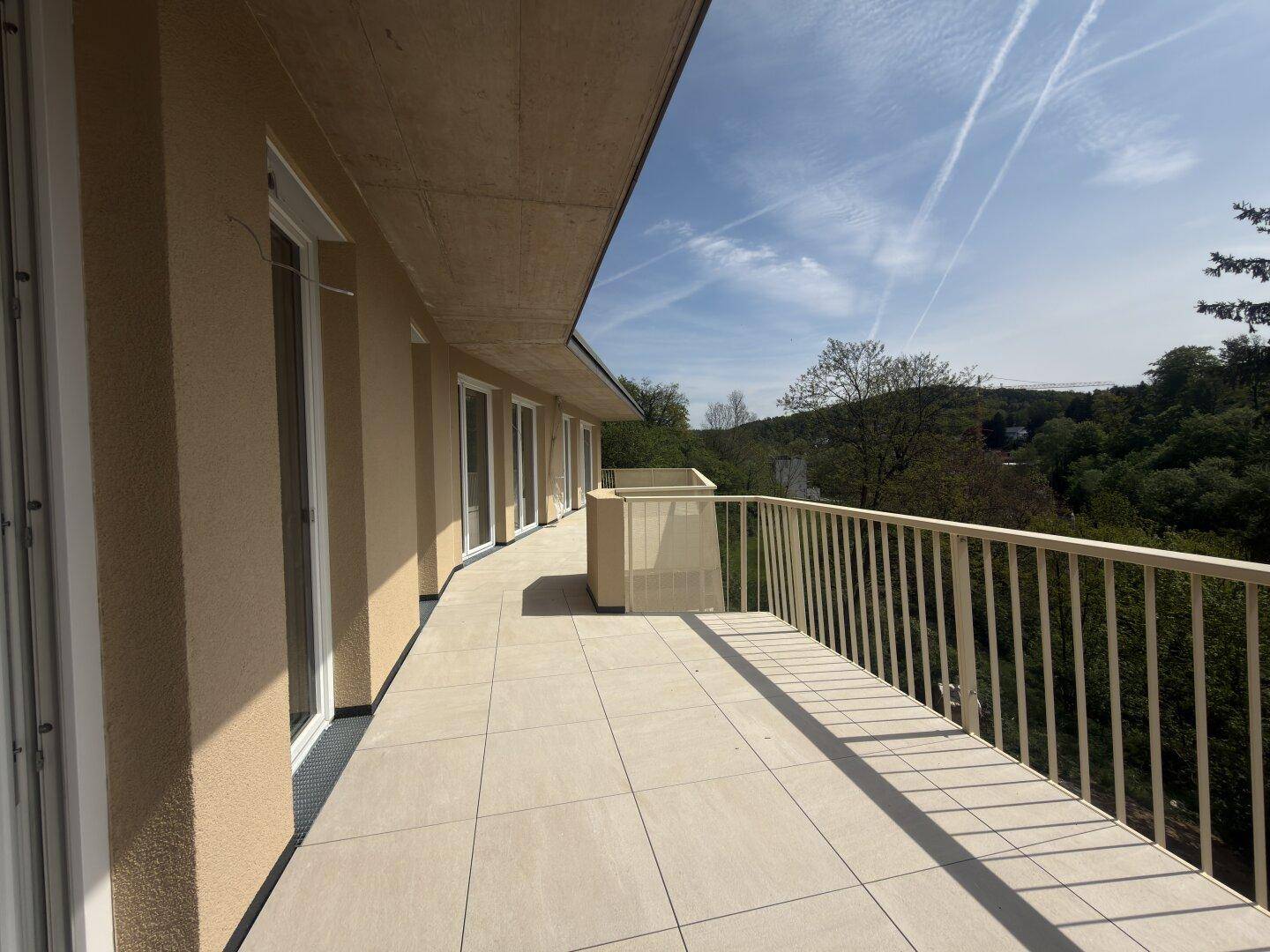 Lange, geflieste Terrasse mit hellem Geländer und weitem Blick auf die bewaldete Landschaft.