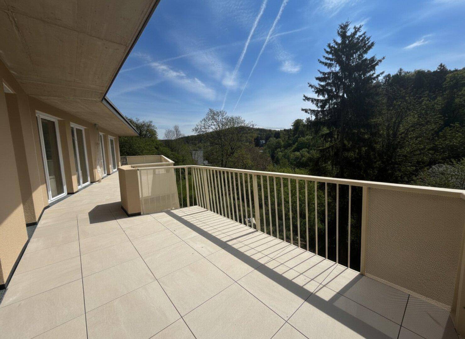 Geräumige, geflieste Terrasse mit weitem Blick ins Grüne und auf bewaldete Hügel.