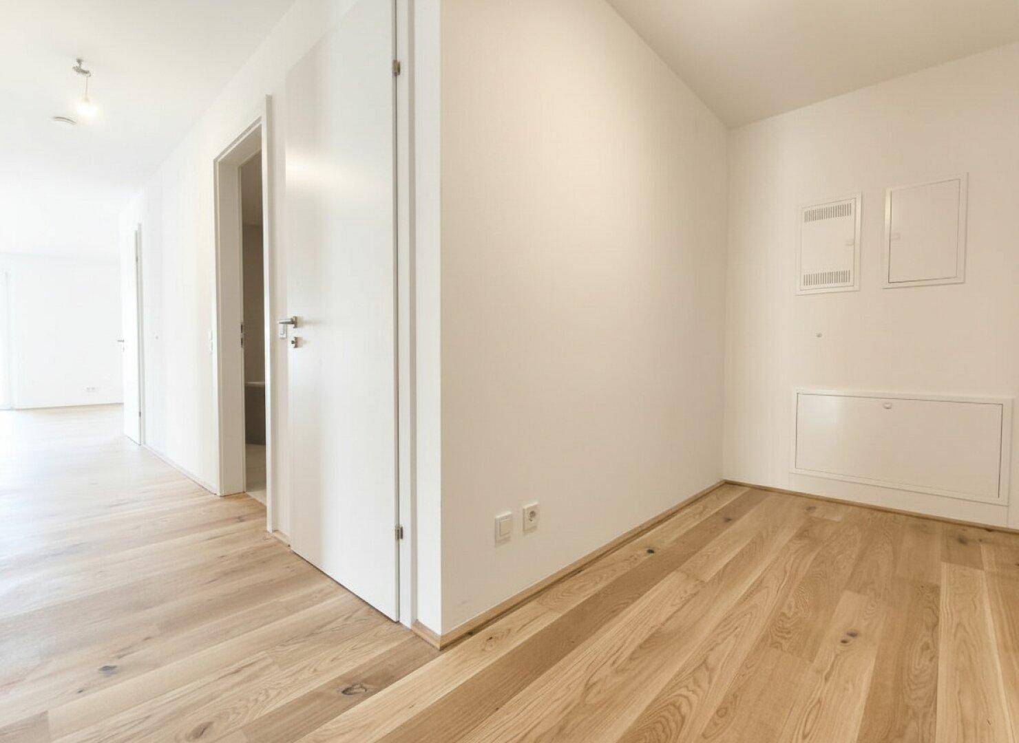 Heller Flur mit Holzboden und weißen Türen, der zu weiteren Räumen führt.