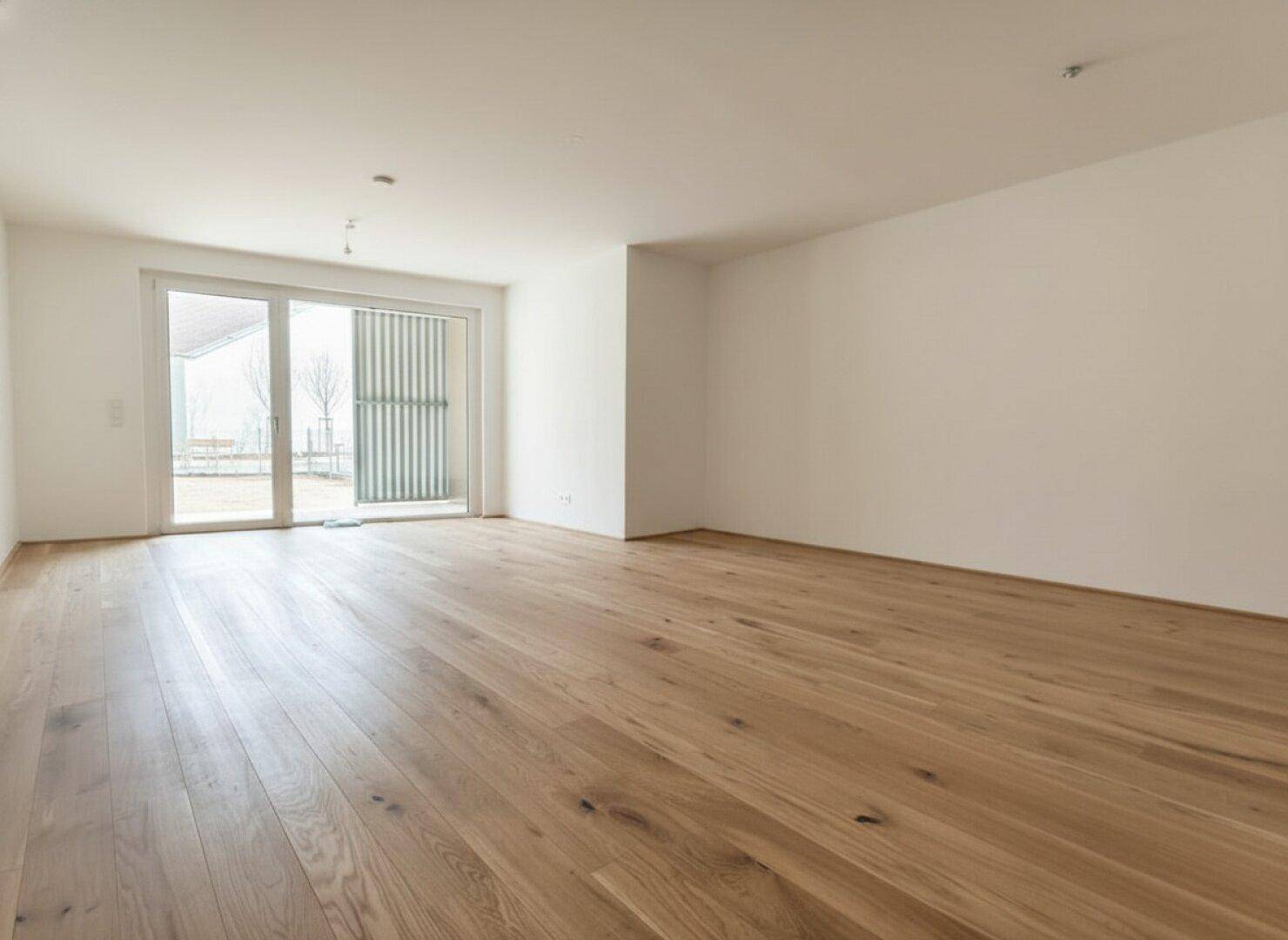 Lichtdurchfluteter Wohnbereich mit eleganten Holzdielen und einer großen Schiebetür zum Außenbereich.