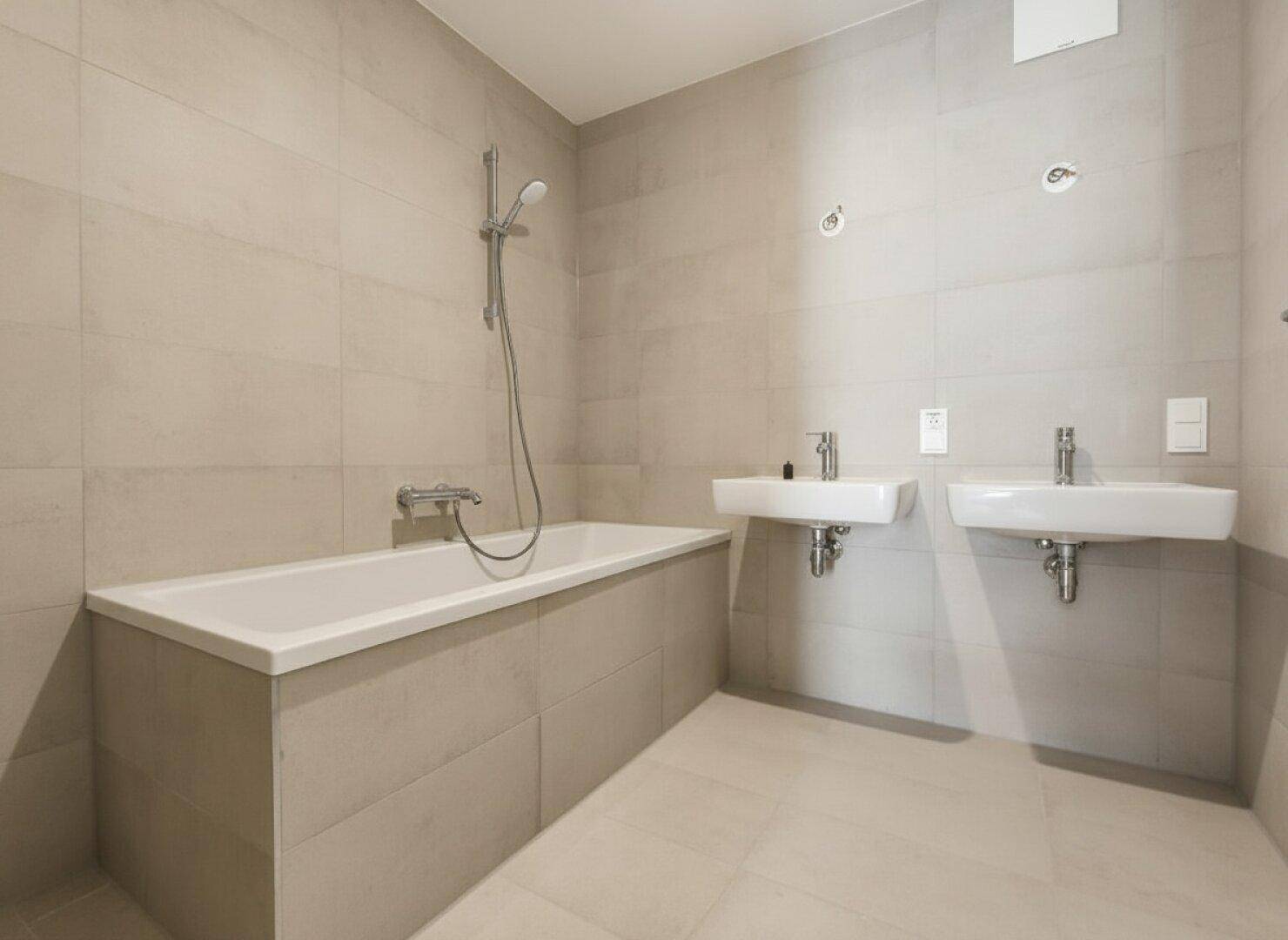Elegantes Badezimmer mit hellen Fliesen, einer Badewanne und zwei modernen Waschbecken.