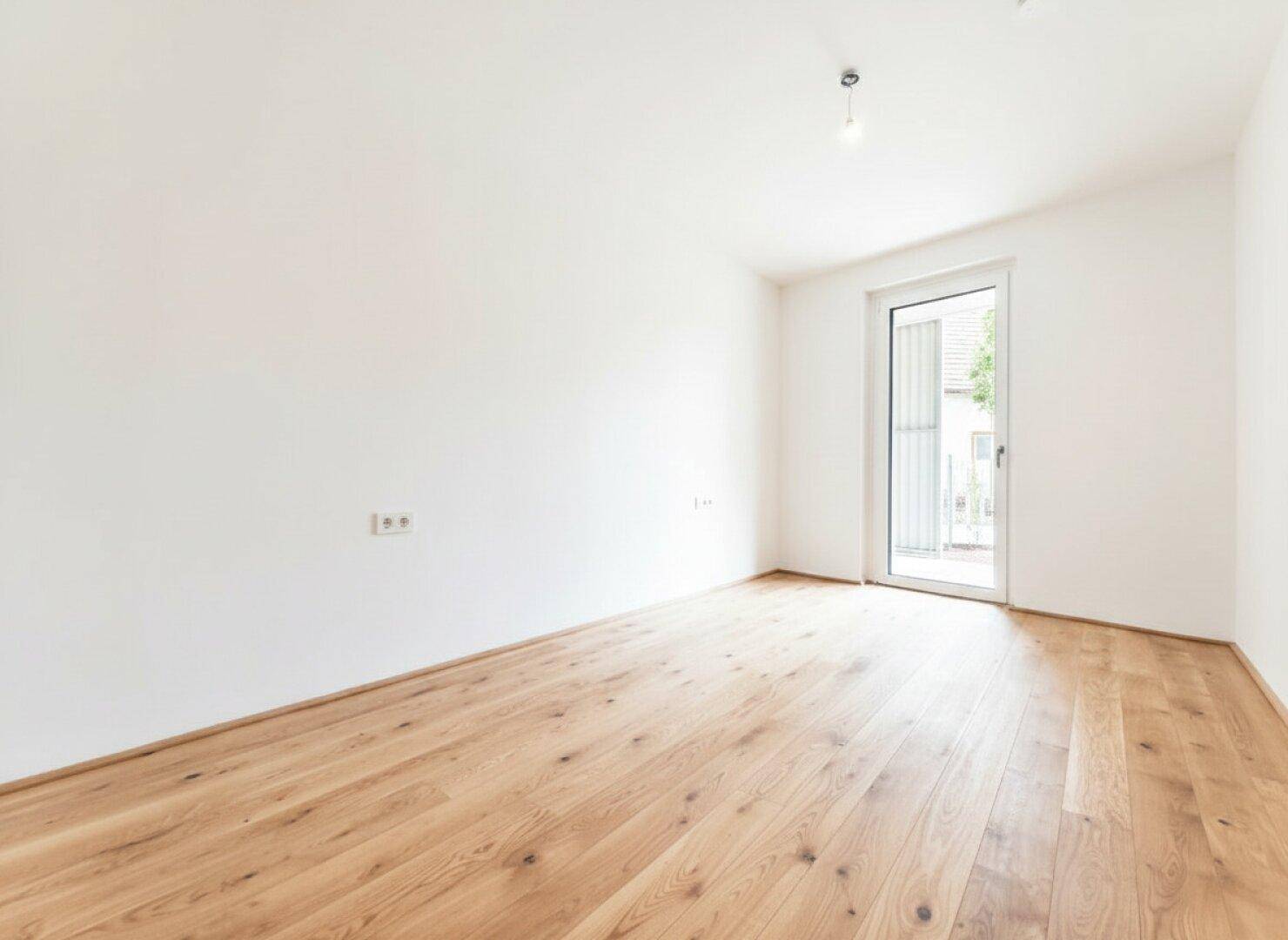 Lichtdurchfluteter Raum mit Holzdielen und einer Glastür, die den Zugang zum Außenbereich ermöglicht.