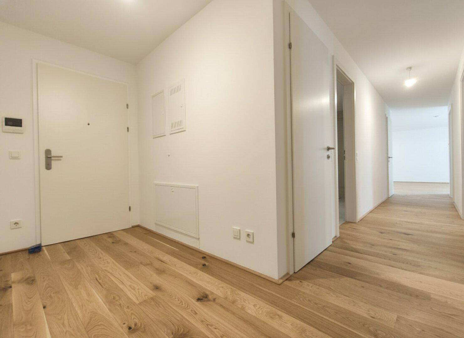 Heller Flur mit Holzdielenboden und mehreren weißen Türen, die zu den Zimmern führen.