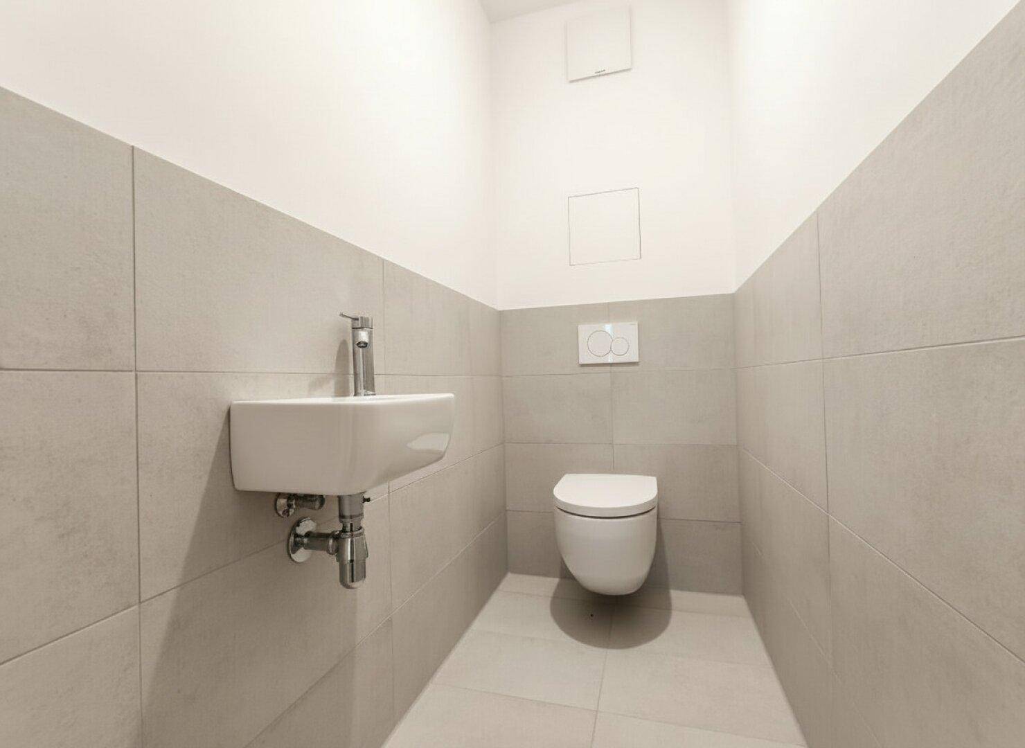 Gäste-WC mit modernen hellgrauen Fliesen, wandhängendem WC und kleinem Waschbecken.