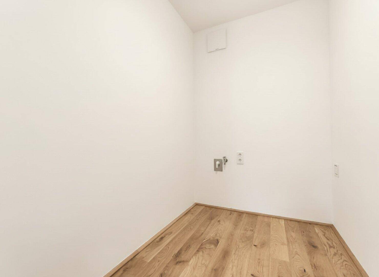 Praktischer Hauswirtschaftsraum mit Holzdielenboden und Anschlüssen für Waschmaschine.