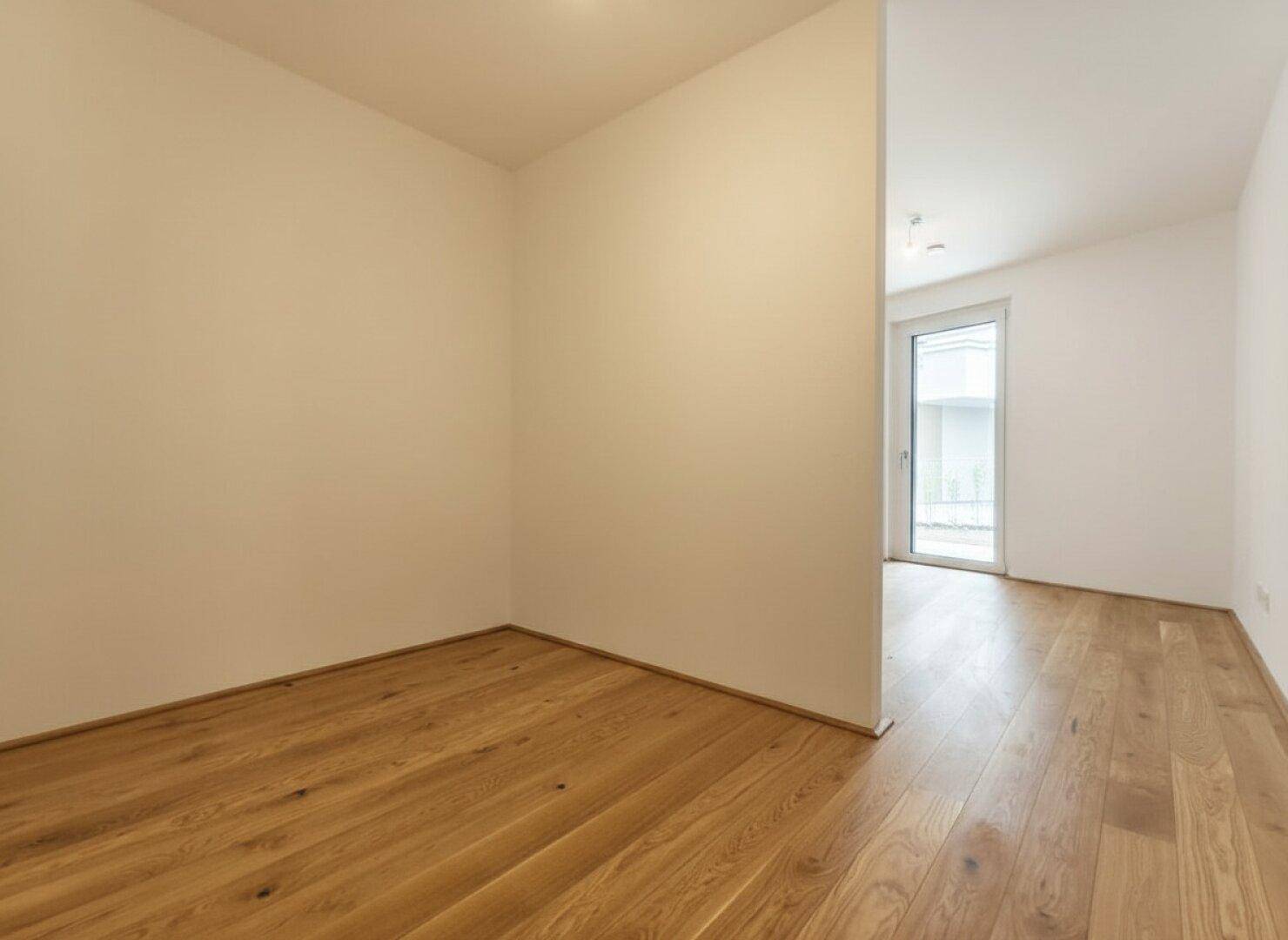 Helles Zimmer mit Holzfußboden und weiß gestrichenen Wänden, mit Zugang zum Außenbereich.
