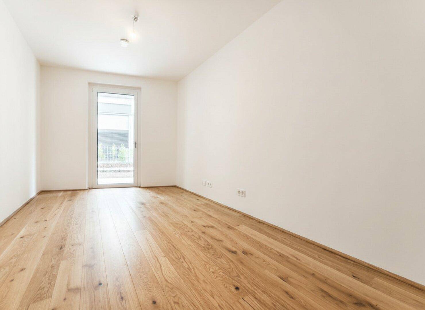 Helles Zimmer mit Holzfußboden und weiß gestrichenen Wänden, mit Zugang zum Außenbereich.