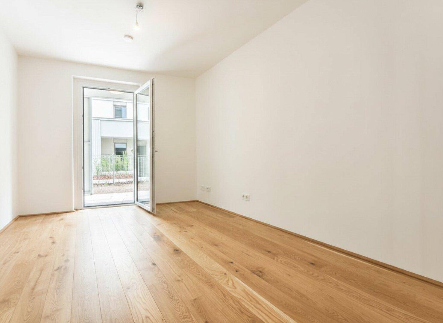 Helles Zimmer mit Holzfußboden und offener Tür, die den Blick auf den Außenbereich freigibt.