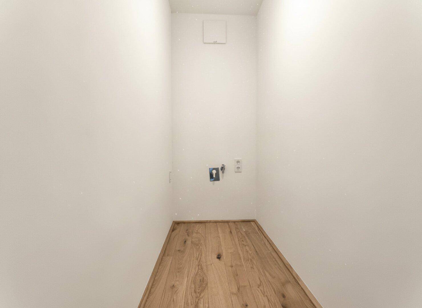 Kleiner Hauswirtschaftsraum mit Holzfußboden und Anschlüssen für Waschmaschine oder Trockner.