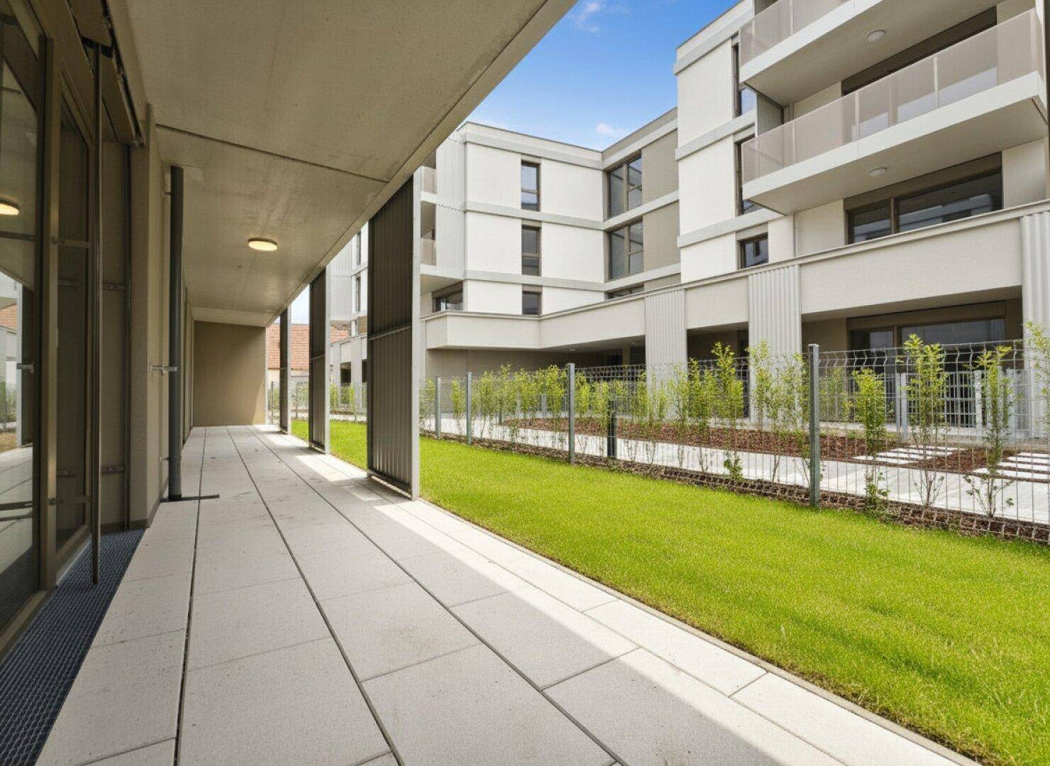 Moderne Außenanlage mit gepflasterter Terrasse, Rasen und Blick auf die Fassade des Wohngebäudes.