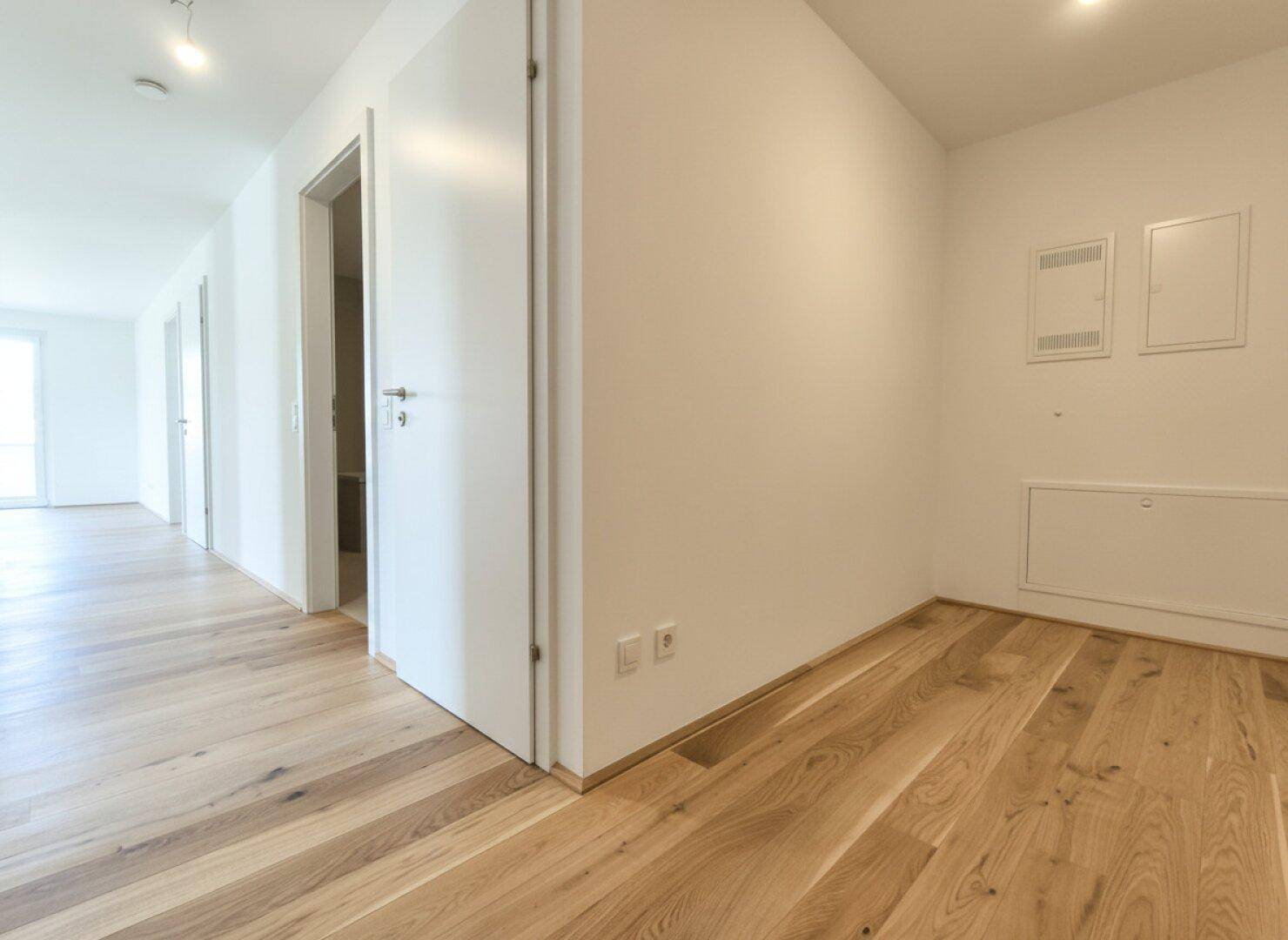 Heller Flur mit Holzboden und weißen Türen, der zu verschiedenen Räumen führt.