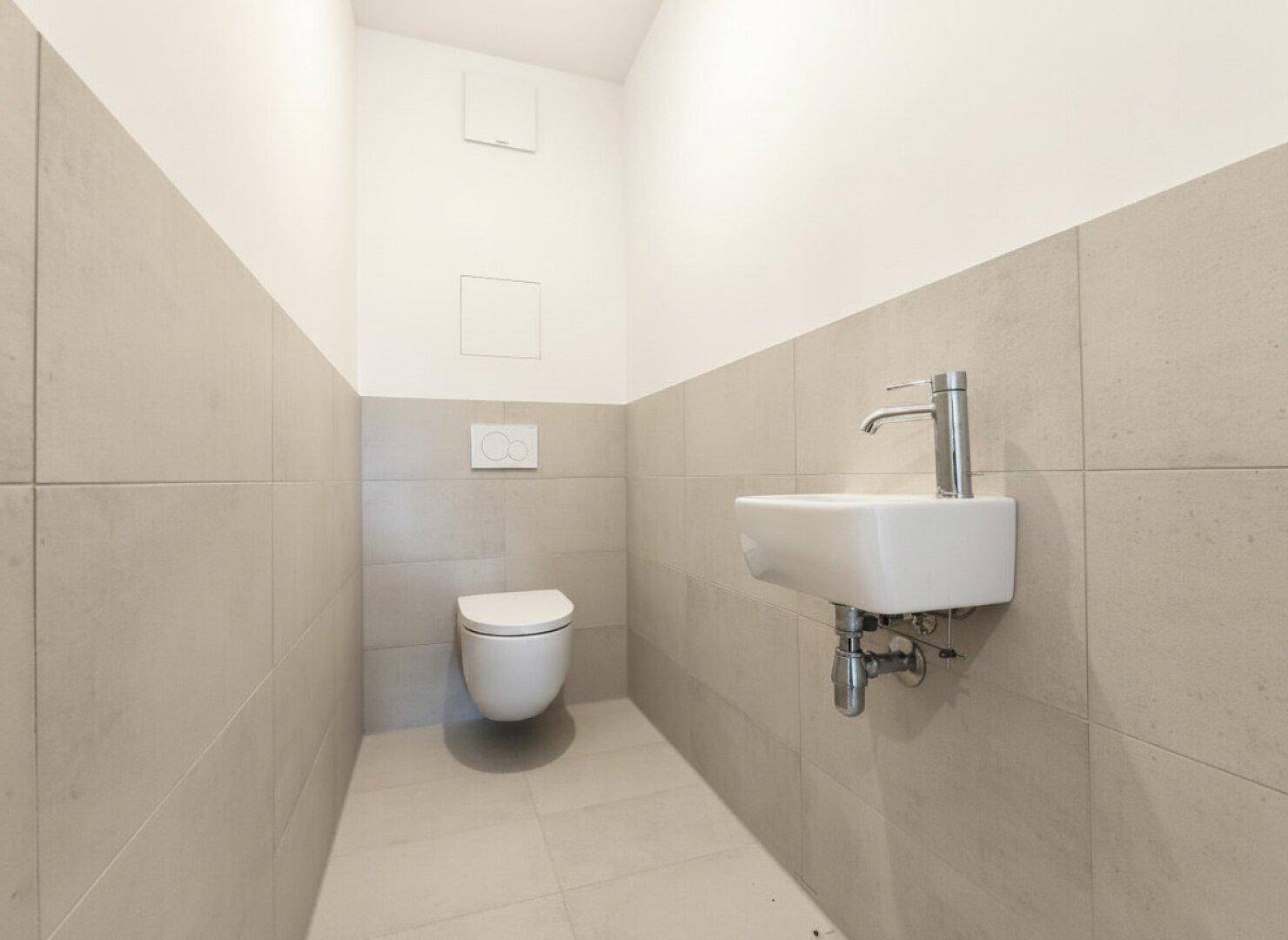 Kleines Gäste-WC mit modernem wandhängendem WC und Handwaschbecken, halbhoch gefliest.