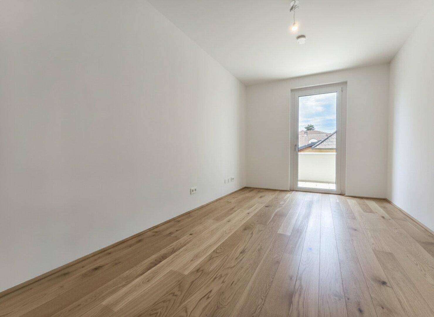 Geräumiges Zimmer mit Holzboden und Zugang zu einem Balkon, bietet viel natürliches Licht.