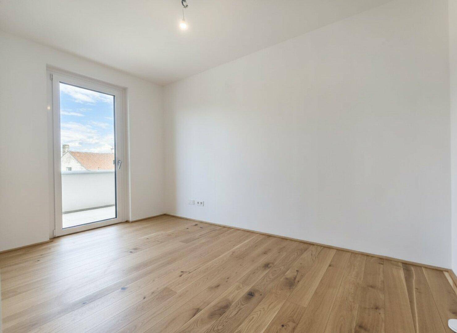 Helles Zimmer mit Holzboden und Balkonzugang, ideal als Schlafzimmer oder Arbeitsbereich.
