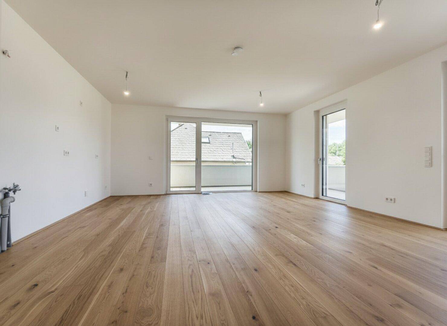 Großes, leeres Zimmer mit hellem Holzboden und Zugang zu einem Balkon, bereit zur individuellen Gestaltung.