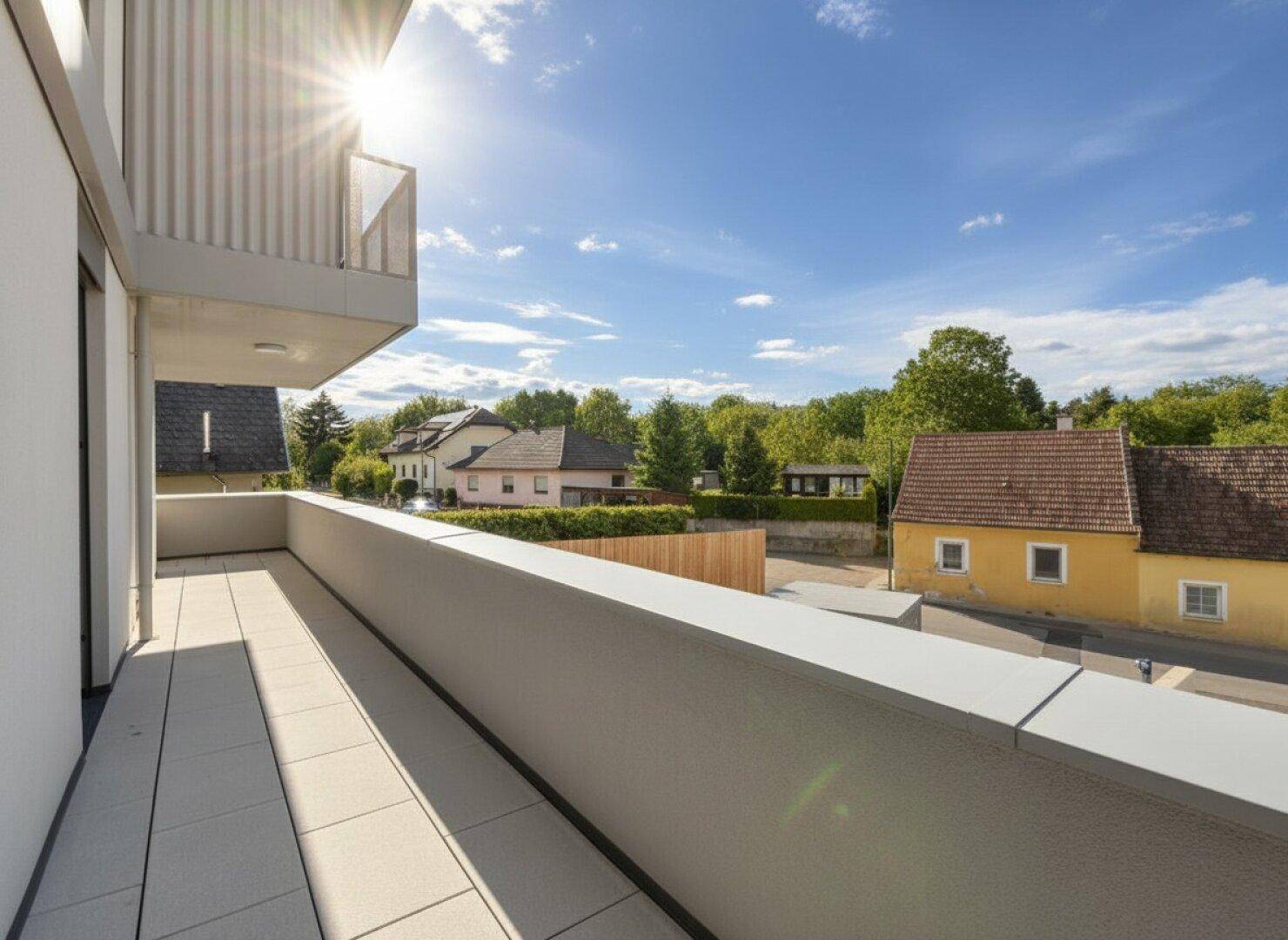 Sonniger Balkon mit Fliesenboden und Blick auf die umliegende Wohngegend und viel Grün.