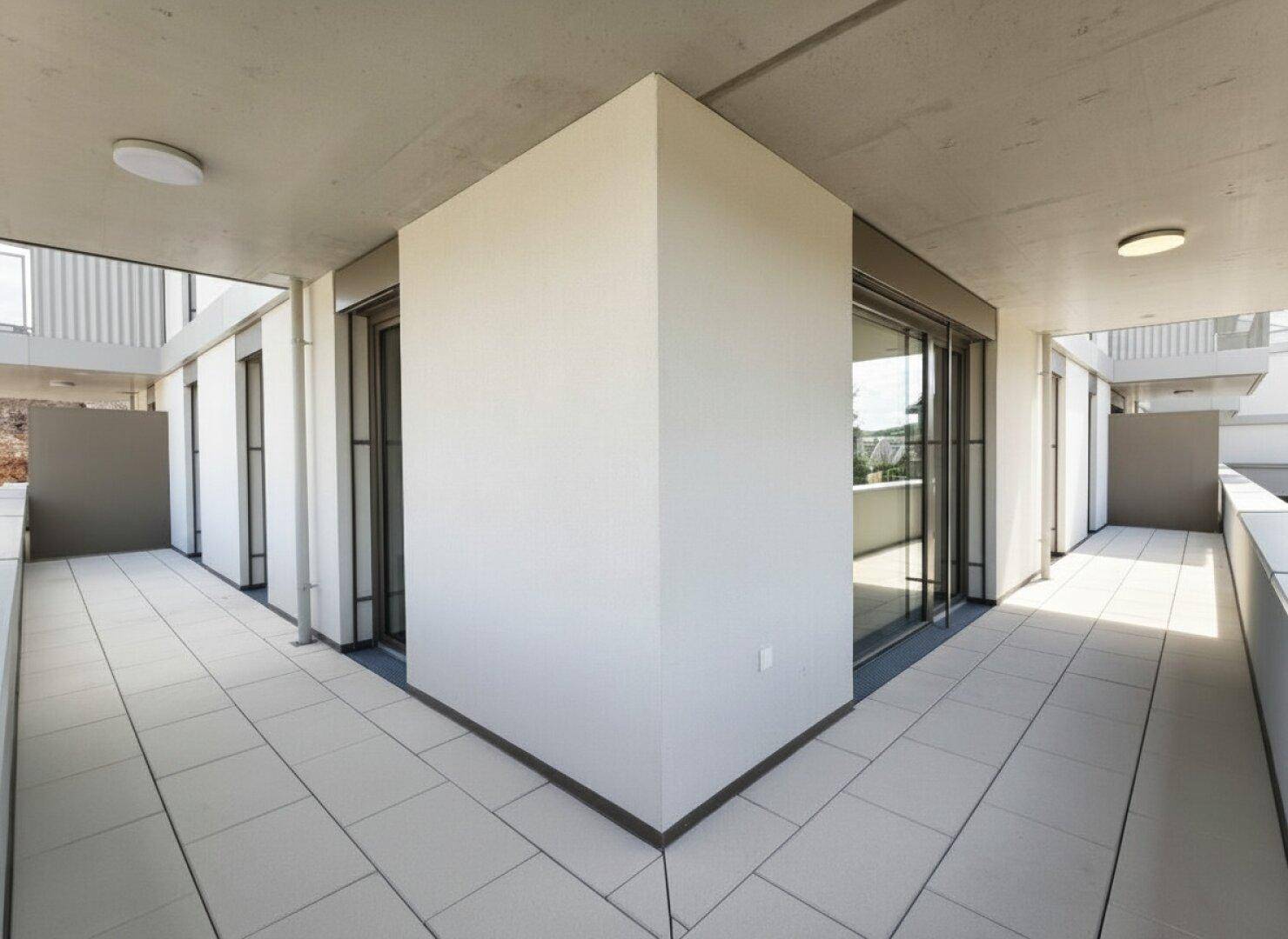 Moderner Eckbalkon mit Fliesenboden und weitem Blick, umgeben von zeitgenössischer Architektur.