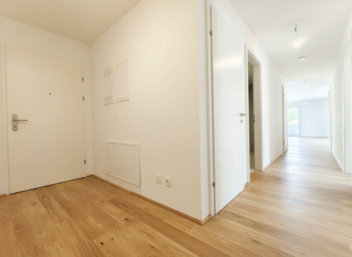 Heller Flur mit Eichenparkett und weißen Wänden, der zu verschiedenen Räumen führt.