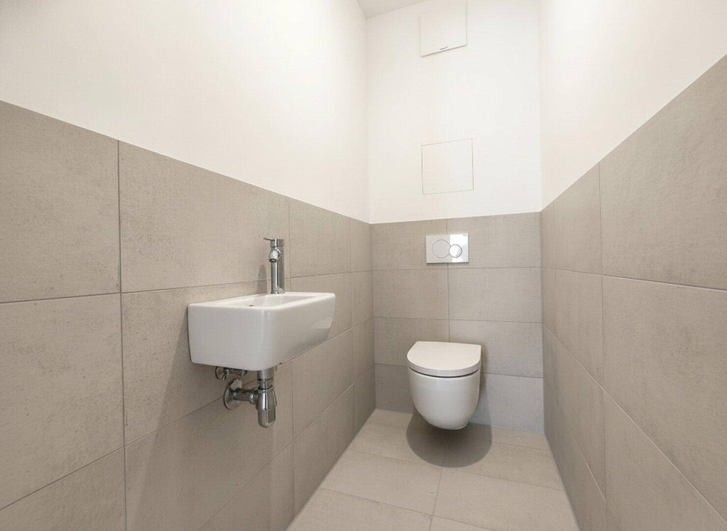 Gäste-WC mit modernen beigefarbenen Fliesen, wandhängendem WC und kleinem Waschbecken.